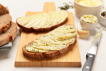 Wooden board of bread slices with fresh butter and garlic on white background