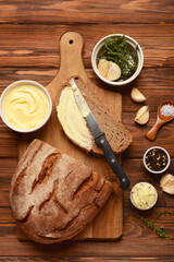 Board of fresh bread with different spices and bowls of butter on wooden background