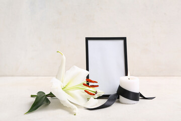 Blank funeral photo frame, candle and white lily on light background