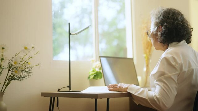 Asian senior mature woman using laptop computer with internet for e-Learning study or business work on desk at home. Elderly people smart life with wireless technology and digital gadget device.