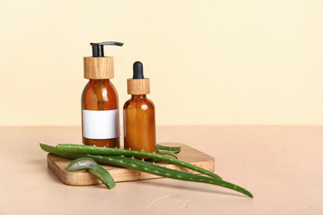 Wooden tray and bottles of aloe vera essential oil on beige background