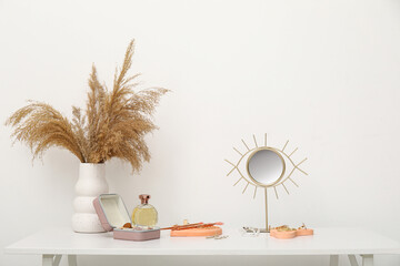 Stylish different jewelry with mirror and vase of pampas grass on table near white wall