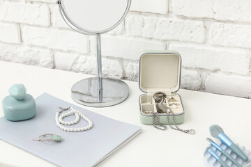 Box with stylish different jewelry and mirror on dresser near white brick wall