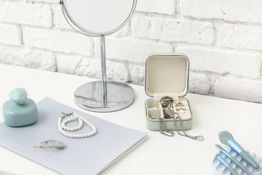 Box with stylish different jewelry and mirror on dresser near white brick wall