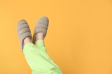 Female feet in slippers near orange wall at home