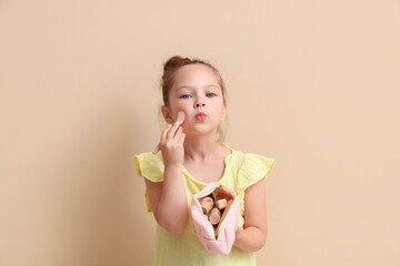 Cute little girl with cosmetic bag and makeup brush on brown background