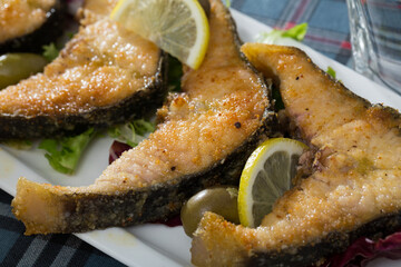 Slices of fried in flour sturgeon served with lemon and olives