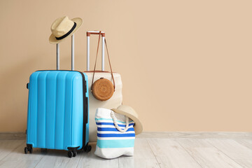 Packed suitcases, hat and beach bag near beige wall