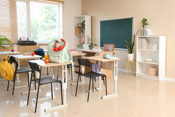 Interior of empty classroom with chalkboard, shelf units and desks