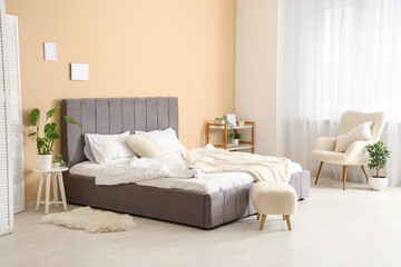 Obraz premium Comfortable bed, armchair, pouf and plant in bedroom