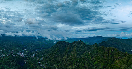 Aerial view Kabut Pelangi Waterfall in East Java. The waterfall stream flows into the mountain gorge in a long path.Above is the residence of the villagers. Abundance of forests on the green mountain.