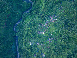 Aerial view Kabut Pelangi Waterfall in East Java. The waterfall stream flows into the mountain gorge in a long path.Above is the residence of the villagers. Abundance of forests on the green mountain.
