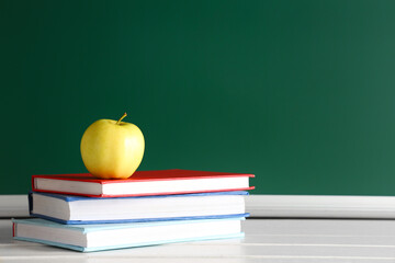 Apple and books on desk near chalkboard. Back to school concept