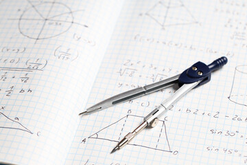 Copybook with handwritten maths formulas and pair of compasses as background, closeup