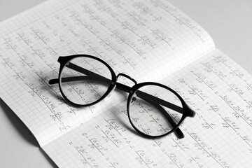 Copybook with handwritten maths formulas and eyeglasses on grey background
