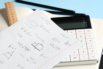 Copybook with handwritten maths formulas and stationery on blue background