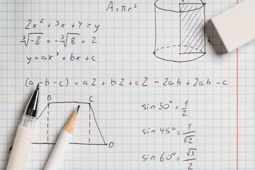 Copybook with handwritten maths formulas and stationery as background, closeup