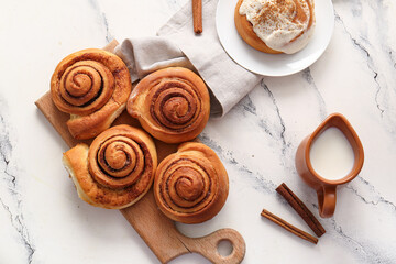 Wooden board and plate with sweet cinnamon rolls on white background