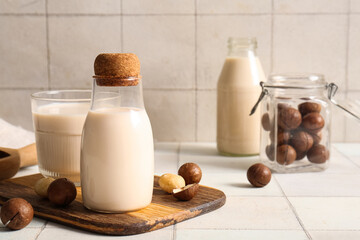 Glass and bottles of fresh macadamia milk on white tile background