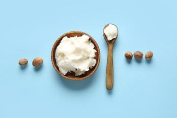 Bowl and spoon of shea butter with nuts on blue background