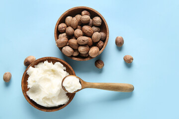 Bowl and spoon of shea butter with nuts on blue background