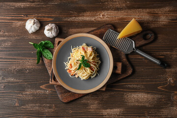 Plate with tasty pasta carbonara, grater and ingredients on wooden background