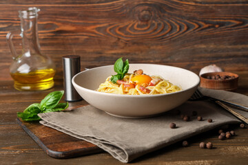 Plate with tasty pasta carbonara, napkin and ingredients on wooden table
