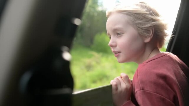 Preteen boy look out through window of car during family road trip and enjoy of pleasant expectation of happy vacation. Glad child travel with parents while holidays. Journey through the countryside