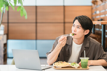 カフェでランチ・パスタを食べる若いアジア人男性
