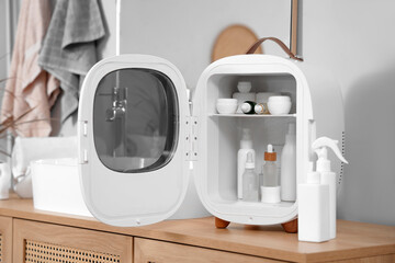 Small refrigerator with cosmetic products on cabinet in bathroom, closeup