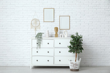 Chest of drawers and houseplant near white brick wall in room