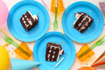 Paper plates with tasty birthday cake, cups and decor on white wooden background