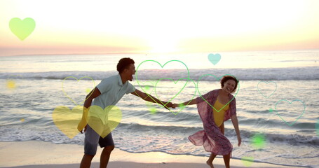 Naklejka premium Image of hearts moving over diverse couple in love dancing on beach in summer