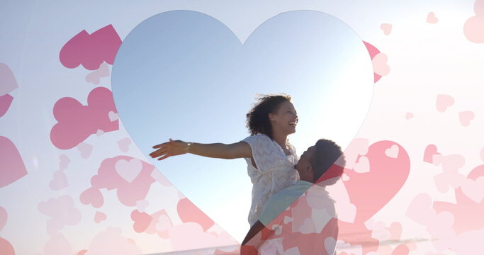 Image of hearts moving over biracial man carrying woman on beach in summer