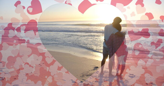 Image of hearts moving over diverse couple in love embracing on beach in summer