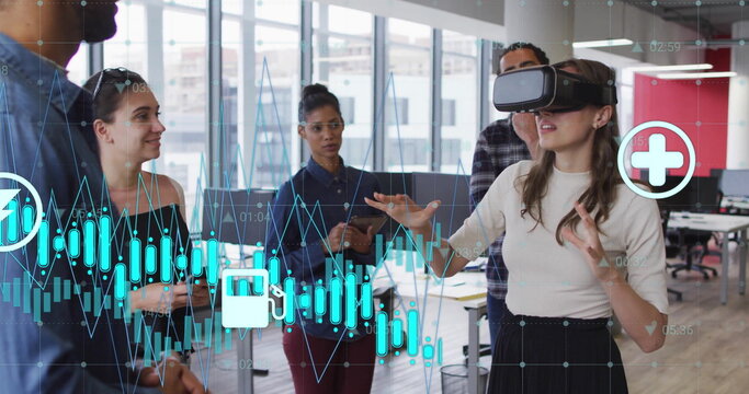 Image of graph and energy icons over diverse colleagues using vr headset at casual office
