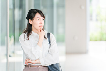 オフィスビルの前で考えるビジネスウーマン（悩み・迷う・困る・不安・不満・心配）
