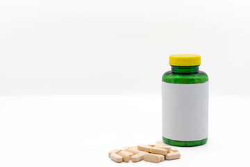Medicine or vitamin bottle with yellow lid and blank label next to yellow pills, isolated on white background with copy space. Selective focus