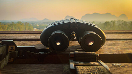 Binoculars lying on the wooden floor The view behind is of the mountains in the morning.