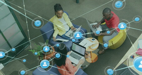 Image of network of connections with icons over diverse colleagues using laptop in office