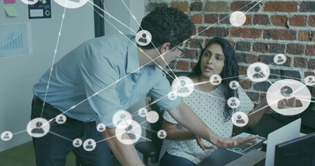 Image of network of connections with icons over diverse colleagues using laptop in office