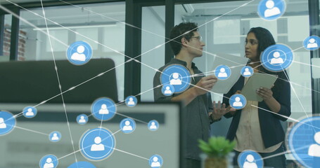 Image of network of connections with icons over diverse colleagues using tablet in office