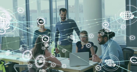 Image of network of connections with icons over diverse colleagues using laptop in office