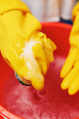 Woman in yellow rubber gloves washing a red bowl with soap and sponge in the sink