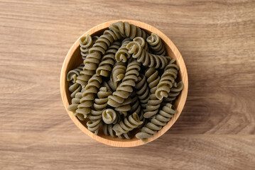 Raw fusilli pasta in bowl on wooden background, Table top view