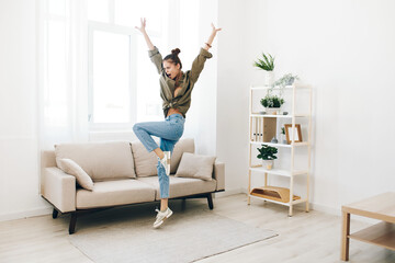 Joyful woman dancing and jumping on the sofa at home, surrounded by music and happiness
