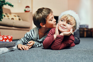 Christmas, kiss and kids waiting for present to celebrate winter holiday, vacation or gift in home. Children siblings, playing or brothers lying on carpet to relax for xmas festive season or love