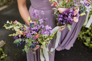 bridesmaids in purple gowns standing outside at summer wedding holding bouquet of colorful florals 