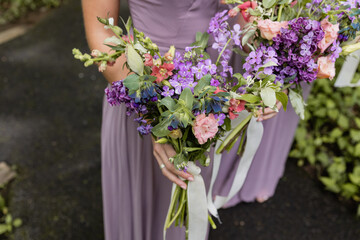 bridesmaids in purple gowns standing outside at summer wedding holding bouquet of colorful florals 