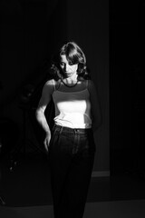 Dramatic portrait of a young woman with long wavy hair, dressed in a white t-shirt and jeans, posing in the shadows and the sunset light.